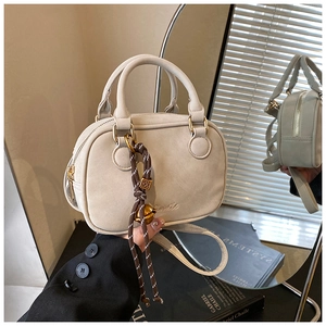 Detailed close-up of a beige mini Boston bag with decorative knot charm and metal bell