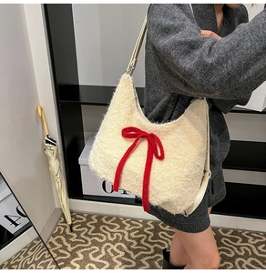Detail of plush off-white crescent hobo bag with a prominent red bow and leather strap