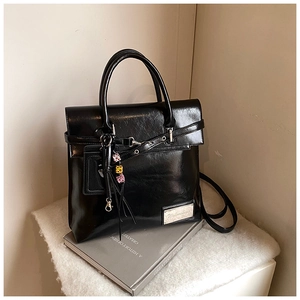 Détail d'un sac cabas en cuir noir brillant avec logo en métal argenté et breloque colorée