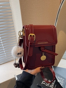 Deep red patent leather mini crossbody bag with gold logo and plush keychain charm