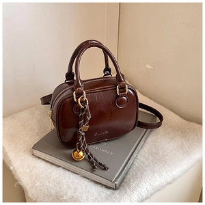 Detail of dark brown glossy leather Boston bag with gold sphere charm and woven strap