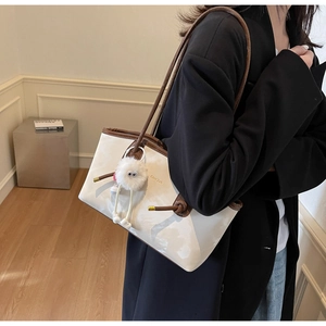 Close-up of a white patent leather tote bag with brown straps and a plush monster charm