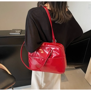Close-up of a glossy red patent leather shoulder bag with decorative buckle on a model