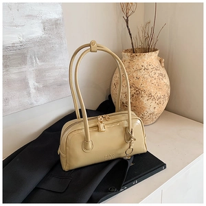 Detail of cream bowling bag with golden lock and sleek leather on black blazer