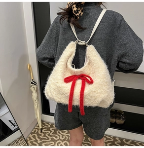 Close-up of fluffy off-white plush shoulder bag with a bold red velvet bow decoration