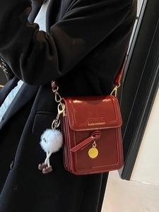 Deep red patent leather crossbody phone bag with gold charm and plush keychain accessory