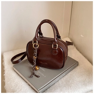 Detail of dark brown vintage Boston bag with glossy finish and decorative pendant
