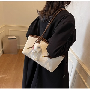 Detail of cream tote bag with brown trim featuring a cute plush pendant and logo