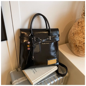Détail du sac à dos en cuir PU brillant noir avec logo doré et breloque perlée