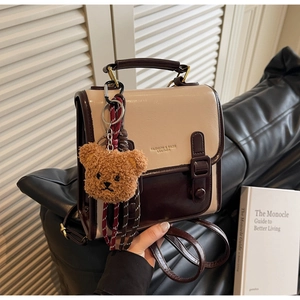 Detail eines Retro-Mini-Rucksacks in Beige und Braun mit Bärenanhänger auf Ledersitz