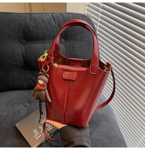 Detail of dark red PU leather bucket bag with a cute bear charm and logo tag