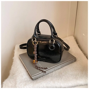 Detail of a black glossy leather mini handbag featuring woven charm and embossed logo