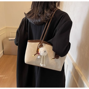 Detailed shoulder view of a two-tone beige and brown tote bag with white plush charm