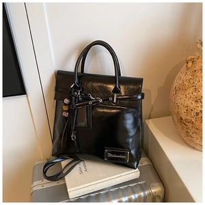 Détail d'un sac cabas en cuir noir brillant avec œillets argentés et breloque perlée