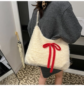 Plush off-white tote bag with a red knitted bow detail worn by a model in a cozy setting