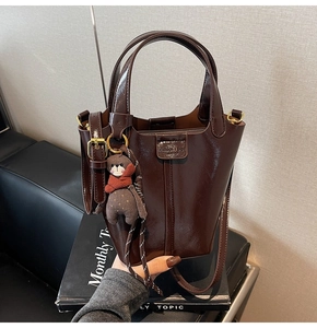 Detail of dark brown glossy bucket bag featuring double handles and cute bear charm