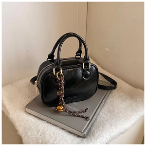 Detail of glossy black bowling handbag with woven bell charm and polished finish