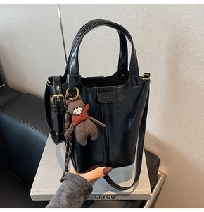 Detail of glossy black bucket bag with a cute brown bear charm and gold hardware accents