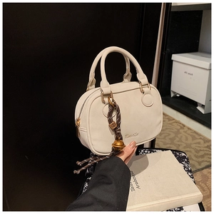Detail of cream white small square bag with golden hardware and bell woven pendant
