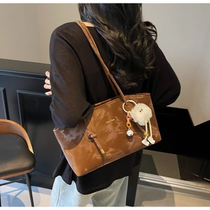 Detail of a brown leather tote bag with gold lettering and a white plush charm on the strap