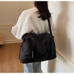 Détail du sac cabas en nylon noir avec bandoulière à lettres blanches porté à l'épaule