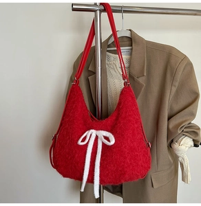 Detail of red plush tote bag with white knitted bow accent on a khaki blazer