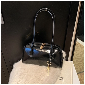 Macro detail of glossy black leather bowling bag featuring golden padlock and key accents