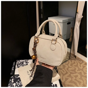 Detail of cream-colored shoulder bag with gold bell charm and Komilio logo engraving