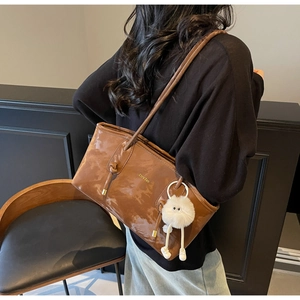 Brown faux leather tote bag detail with gold logo and plush doll charm on strap