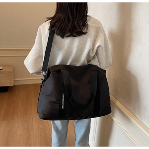 Détail du grand sac cabas en nylon noir avec bandoulière lettrée porté à l'épaule