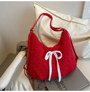 Close-up of red plush shoulder bag with white bow and adjustable leather strap