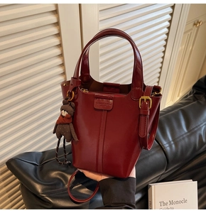 Detail of burgundy leather bucket bag featuring a mini bear charm and embossed logo tag