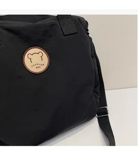 Dettaglio della borsa a tracolla in nylon nero con stemma di orso e tracolla larga