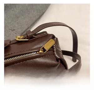 Détail macro du sac en cuir marron foncé montrant le zip doré et la boucle métallique