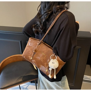 Glossy brown tote bag detail with double straps and plush monster keychain accessory