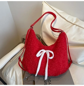 Detail of red plush hobo bag featuring a white rope bow on a white leather sofa