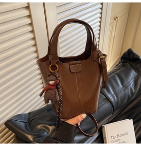 Detail of dark brown leather bucket bag with cute bear charm and adjustable strap