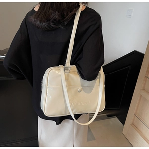 Detail view of cream patent leather shoulder bag with embossed logo and glossy finish