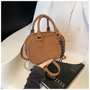 Detail of a brown vintage crossbody bag with a decorative bell pendant and gold zipper
