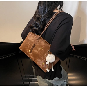 Detail of dark brown tote bag with gold logo, knotted strap and plush monster charm