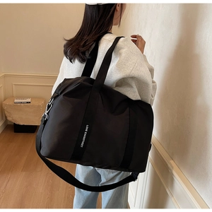 Détail du sac cabas en nylon noir avec sangle lettrée blanche et mousquetons en métal