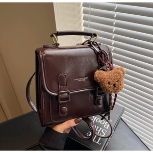 Nahaufnahme eines braunen Vintage-Lederrucksacks mit Schnallen und einem Plüschbär-Anhänger