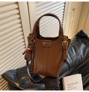 Detailed view of a brown PU bucket bag with bear pendant on a leather sofa