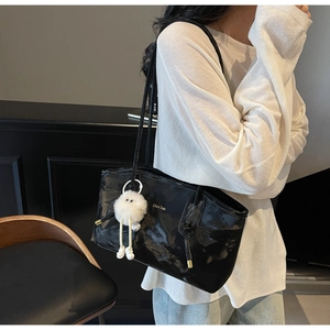 Detail of black glossy leather tote bag with gold lettering and plush doll charm