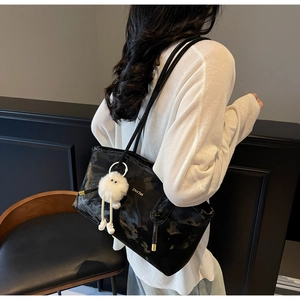 Black glossy tote bag with dual straps and a white plush monster charm detail