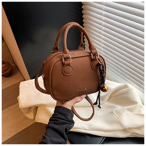 Close-up of brown textured bowling bag with gold bell charm and braided knot detail
