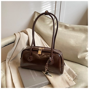 Detail of glossy dark brown leather bowling bag with gold lock on a beige blazer