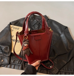 Detail of burgundy bucket bag with plush bear charm on black leather background
