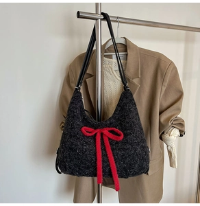 Detail view of plush black tote bag featuring a vibrant red bow accent and thin strap