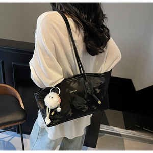 Macro shot of glossy black patent leather tote bag with white faux fur charm and logo